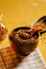 Buckwheat groats in a wooden bowl with steam rising against a yellow backdrop