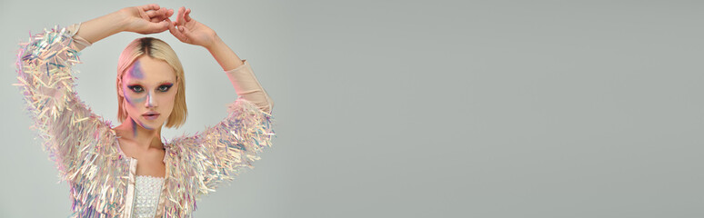 Blonde young woman in stylish party outfit poses with holographic elements in studio
