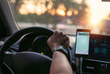 Person driving a car at sunset while using a smartphone GPS navigation app on the dashboard for real-time route guidance and travel direction.