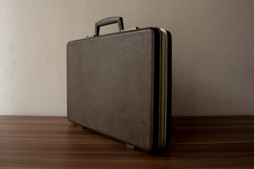 Dark vintage hard shell rectangular briefcase on the wooden table. This bag is durable and waterproof, making it suitable for storing important documents, especially those related to business. 