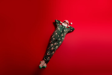 Relaxed Santa in festive pajama lounge on red background enjoying holiday mood and Christmas joy for seasonal home use