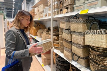Side view of Caucasian young female customer choosing home decoration in store. Beautiful woman looking and holding in hands decorative basket for storage of things at home
