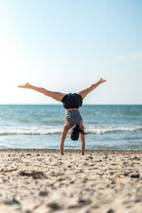 Joyful female athlete performing acrobatic move at coast, Playful lady showcasing athleticism with cartwheel by ocean