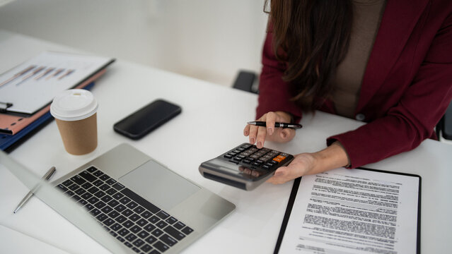 Asian adult woman calculating property finance business on office desk with laptop documents coffee cup sales analysis planning strategy