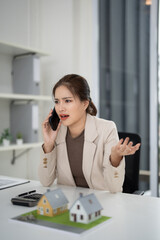 Asian adult real estate agent discuss property details phone call office house models property...