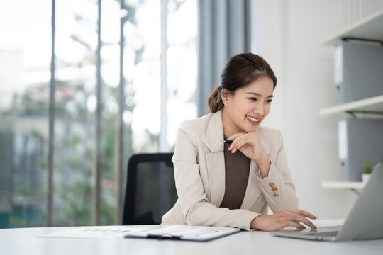 Asian real estate agent woman working laptop modern office managing property sales happy business professional digital marketing client communication