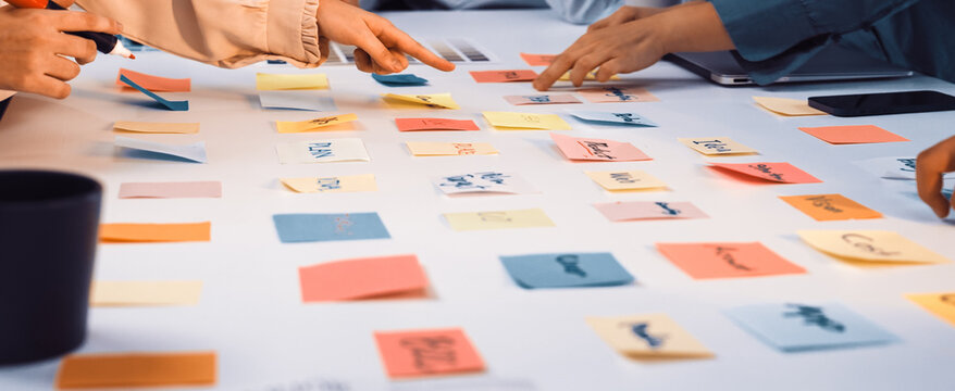 A vibrant scene of diverse hands reaching for colorful sticky notes on a white table, highlighting creative collaboration and brainstorming in a modern workspace setting. SACTR