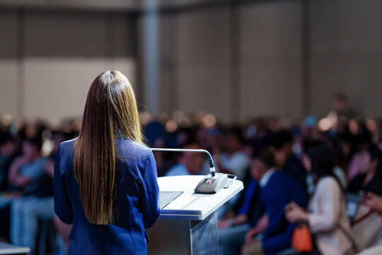Rear view of woman speaker giving an inspiring talk or leading a workshop for young professionals and adult training participants in a large conference room.