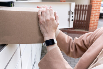 Woman retrieving a package from a delivery box while wearing a smartwatch during the day