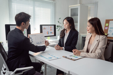 Fototapeta premium Business team members collaborating and discussing financial data charts and graphs on a clipboard and computer screens during an important meeting in a corporate office setting