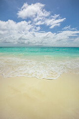 Sunny Summer Beach Landscape with Calm Blue Sea Waves washing on White Sand. Minimal and Tranquil Tropical Mediterranean Background under a Bright Sky. Relaxing and Perfect for Exotic Holiday Travel