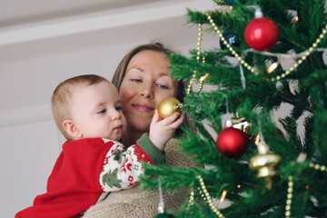 Mom and her newborn decorating a Christmas tree together. Copy space, background.