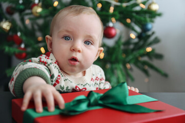 Cute little baby opening the Christmas present. Close up, background.
