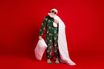 Naklejka na ściany i meble Playful Santa in festive pajama with blanket and pillow against a bold red backdrop