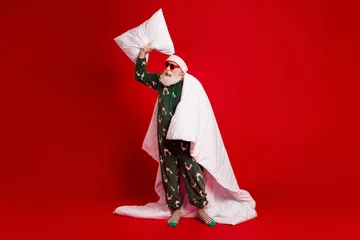 Fotobehang Beren Santa in festive pajama poses with pillow under a red background wrapped in a white blanket for a humorous Christmas stock photo  © deagreez