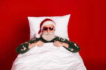 Fotobehang Beren Santa relaxes in a cozy red bedroom wearing a festive pajama sweater and lounging in bed for a playful Christmas photo  © deagreez