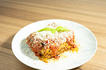 Home mad lasagna Bolognese on a white plate and a wooden background.