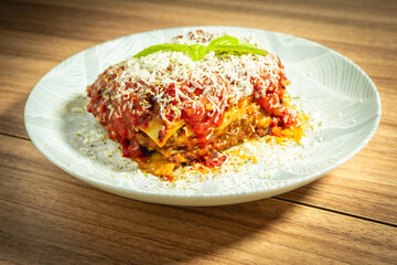 Home mad lasagna Bolognese on a white plate and a wooden background.