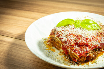 Home mad lasagna Bolognese on a white plate and a wooden background.