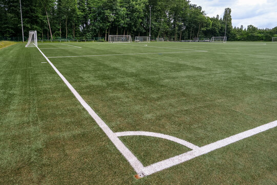 Weiter Blick seitlich von oben auf einen leeren Fu&szlig;ballplatz mit Kunstrasen, wei&szlig;en Markierungen, Toren und Ausr&uuml;stung von Freisto&szlig;ecke aus, viel Copy Space