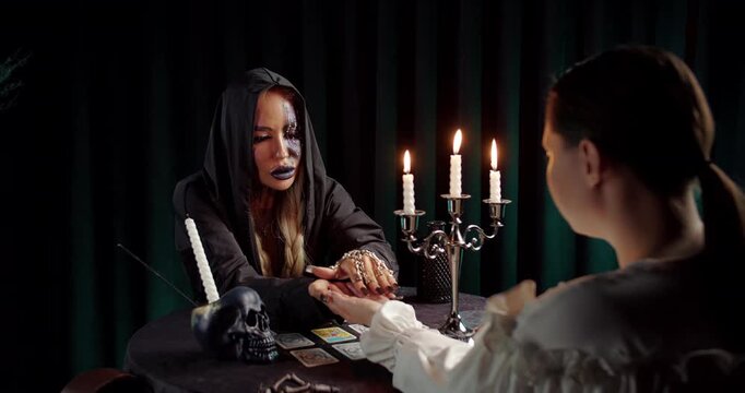 Witch reading clients palm in candlelit fortune telling ritual
