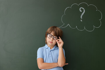 Back to school. Boy near chalkboard with drawn thought bubble and question mark indoors