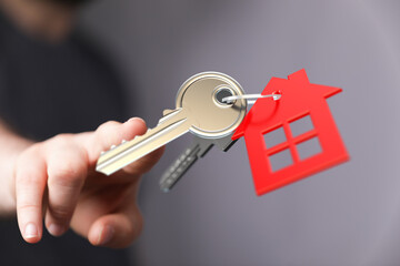 Close-up of a hand holding a set of keys with a house-shaped keyring. Represents property ownership, new home, and the concept of buying or rent