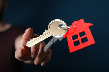 A person's hand presents keys with a house shaped tag, representing home ownership, real estate, and the purchase of a new property.