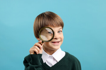 Little boy with magnifying glass on light blue background