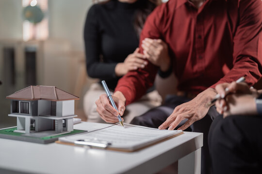 Happy young couple signing mortgage papers with a real estate agent at a table, finalizing a home purchase and investing in their future with smiles and documents