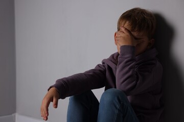 Upset little boy near light grey wall indoors, space for text