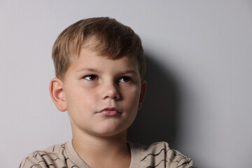Upset little boy crying near light grey wall indoors, space for text