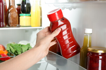 Woman taking bottle of tasty tomato sauce from fridge, closeup