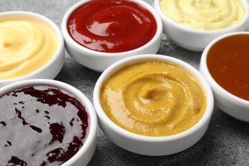 Different tasty sauces in bowls on grey table, closeup