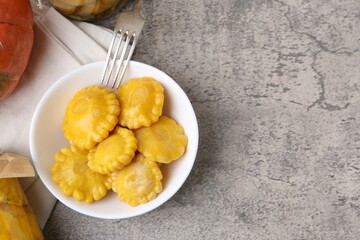 Pickled pattypan squashes in bowl and fork on grey textured table, flat lay. Space for text