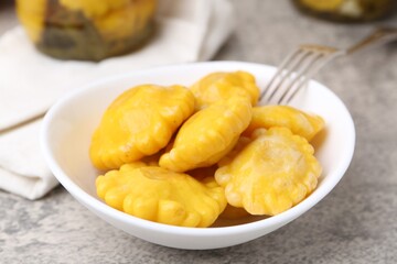 Pickled pattypan squashes in bowl and fork on grey textured table, closeup