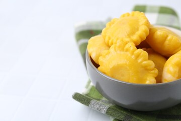 Pickled pattypan squashes in bowl and towel on white tiled table, closeup. Space for text