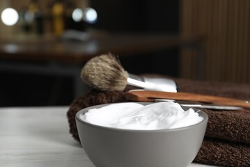 Shaving foam in bowl, straight razor, brush and towel on light wooden table in barbershop, closeup. Space for text