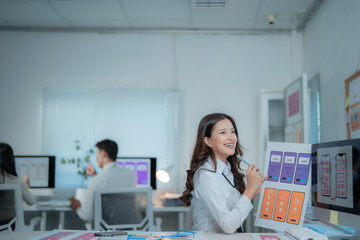 Young woman explaining user interface and experience layouts for a new mobile application, collaborating with colleagues in a modern office environment