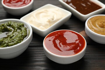 Different sauces in bowls on wooden table, closeup
