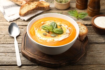 Delicious pumpkin cream soup with basil and seeds served on wooden table, closeup