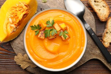 Delicious pumpkin cream soup with parsley served on wooden table, flat lay
