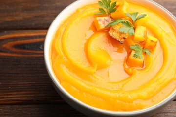Delicious pumpkin cream soup with parsley served on wooden table, closeup