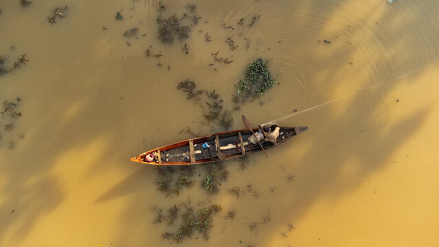 Aerial view of a lone fisherman in a wooden boat, casting a line into the tranquil, ochre-colored water near Alex Ekwueme Way, Abuja, Federal Capital Territory, Nigeria.