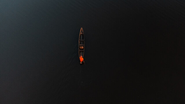 Aerial view of a lone figure in a vibrant orange shirt paddles a slender canoe across the dark, still waters, Alex Ekwueme Way, Abuja, Federal Capital Territory, Nigeria.