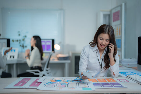 Woman UX UI designer collaborating on user experience and user interface layouts, communicating on a smartphone while developing wireframes and prototypes for mobile applications in an office