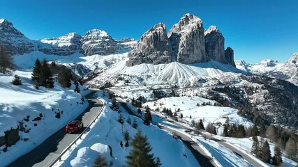 Aerial view of red car driving on winding road through snowy mountains under a clear blue sky day