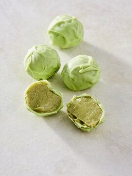 These green candy balls are coated in a smooth layer, revealing a creamy filling when cut in half. Perfect for sweet treats or desserts, they look appealing on a light surface