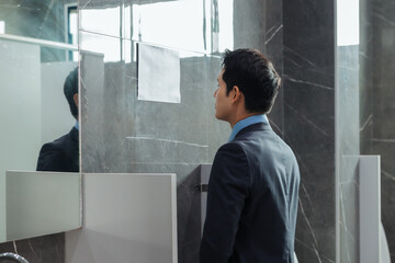 Businessman in a suit looking at his reflection in a public restroom mirror, preparing for work or...