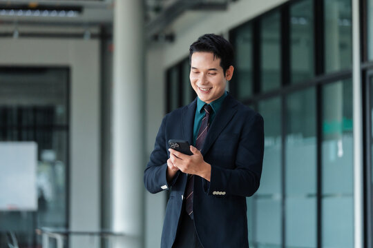 Smiling Asian businessman using a mobile phone, browsing social media or communicating in a modern office environment